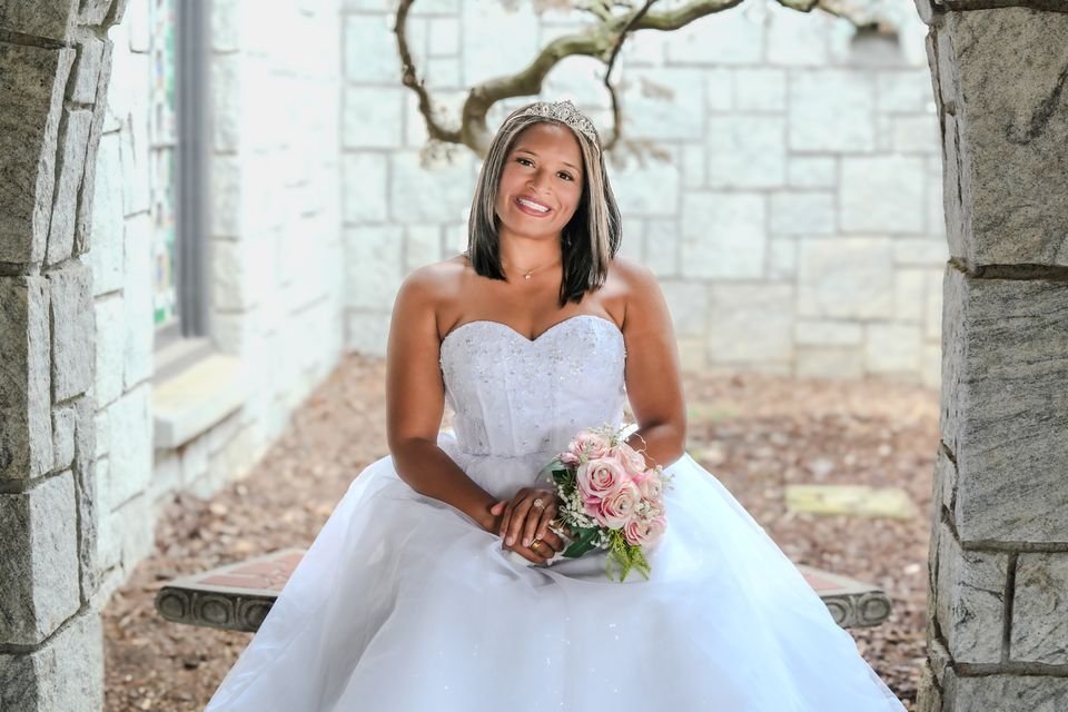 Before: the original color photo of a bride seated under a stone archway holding a rose bouquet.