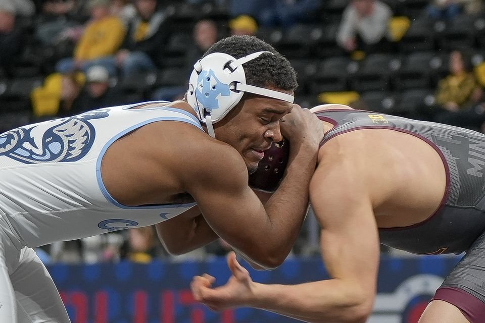 Two collegiate wrestlers locked head to head in a tie-up during a match.