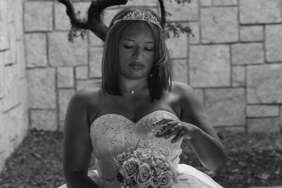 A bride in a tiara looks down at her bouquet, photographed in black and white.