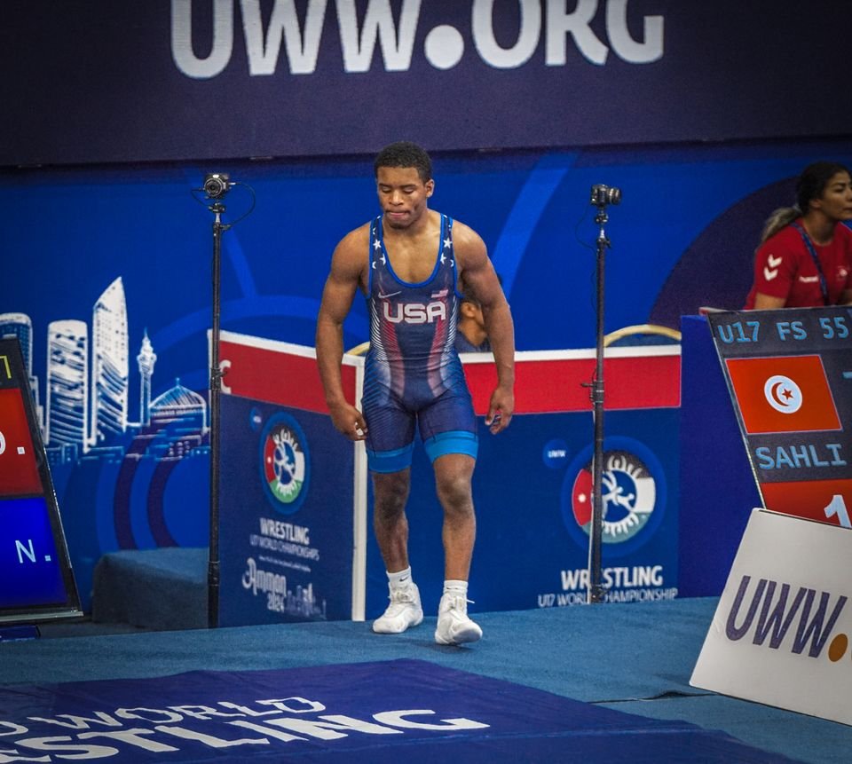 A wrestler in a navy USA singlet walks toward the mat at the U17 World Championships.