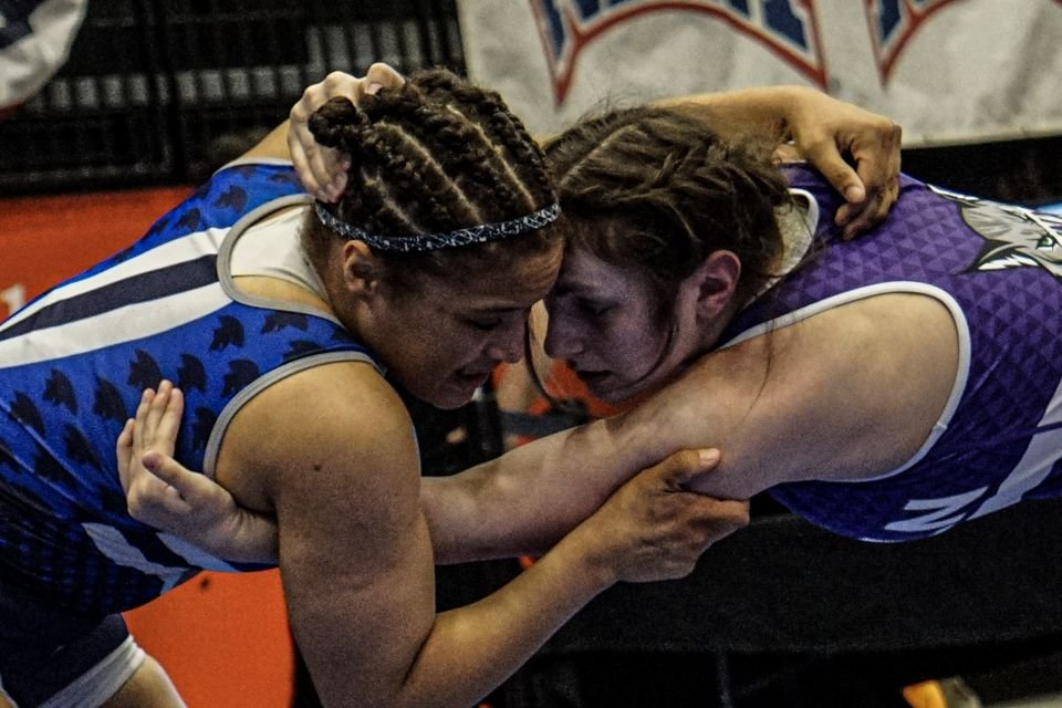 Two women wrestlers lock up chest to chest, faces set in concentration.