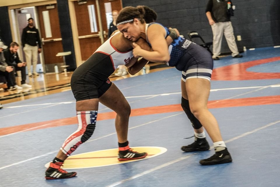 Two women wrestlers in their stance tie up on a blue mat.