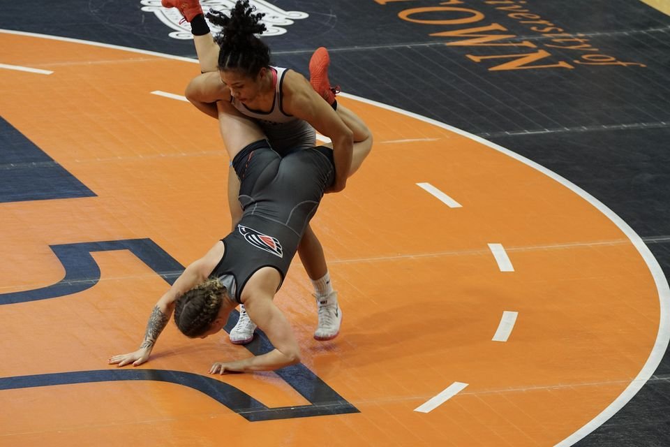 One wrestler lifts another off the orange mat in a high-amplitude throw.