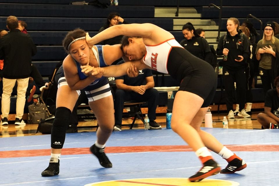 Two women wrestlers hand fight, one gripping the other's wrist.